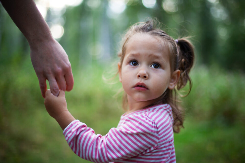 kleines, trauriges und verwirrtes Mädchen an der Hand ihrer Mutter schaut sich nach ihrem Vater um.